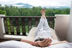 Person relaxing on a cushioned lounger on a balcony overlooking green hills