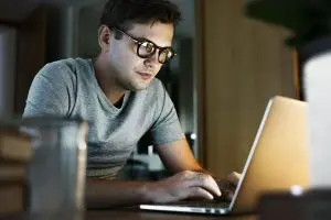 Man in glasses typing on a laptop at night