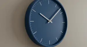 Blue wall clock with white hands against a plain wall